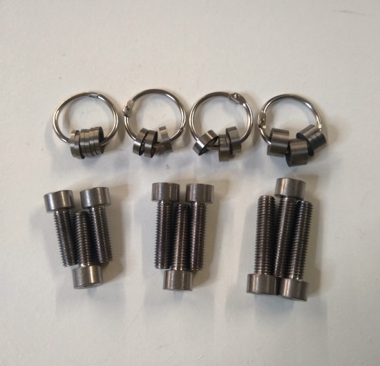 A set of Ski-Doo pDrive Adjustable Pivot Weight Kit TITANIUM bolts and screws on a white surface.